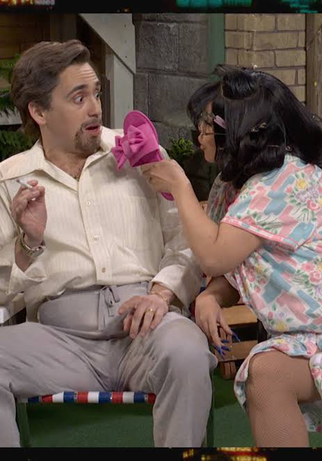 A woman holding a sandal and threatening the seated man beside her